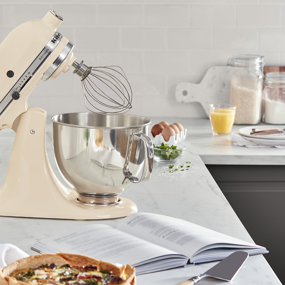 KitchenAid Artisan Series 5-Quart Tilt-Head Stand Mixer in almond cream, on a kitchen counter beside a freshly baked tart