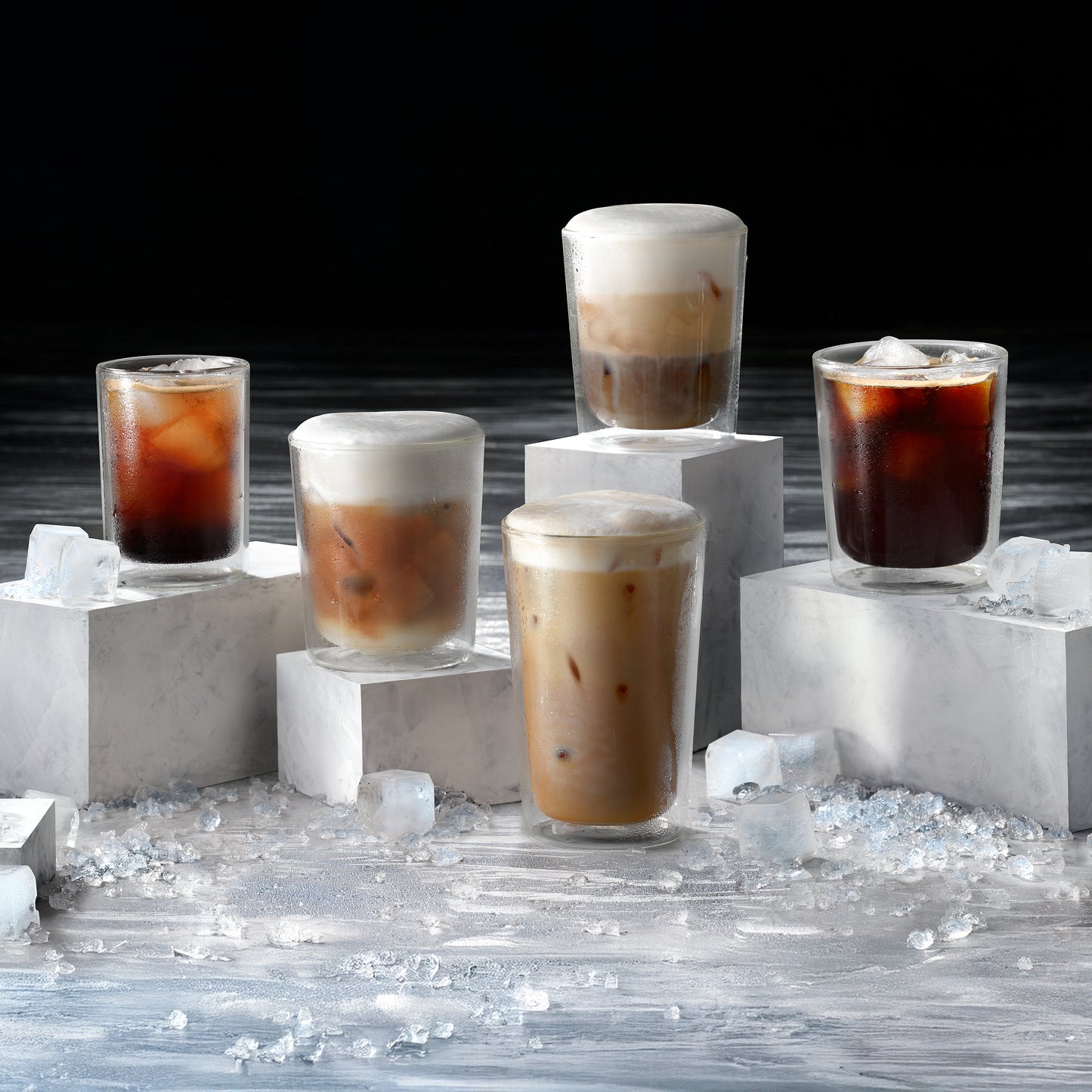 Five glasses of iced coffee on a dark background with ice cubes around.