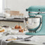 KitchenAid Artisan Series 5-Quart Tilt-Head Stand Mixer in aqua sky, on a kitchen counter beside a dessert spread