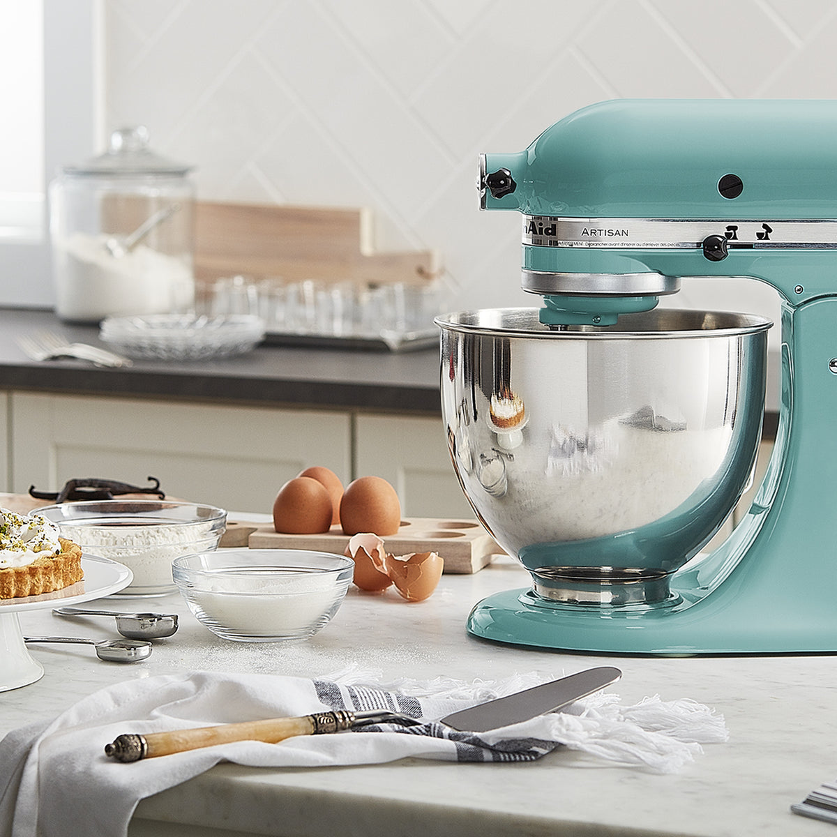KitchenAid Artisan Series 5-Quart Tilt-Head Stand Mixer in aqua sky, on a kitchen counter beside a dessert spread