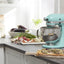 KitchenAid Artisan Series 5-Quart Tilt-Head Stand Mixer in aqua sky, on a kitchen counter with fresh produce and a cutting board
