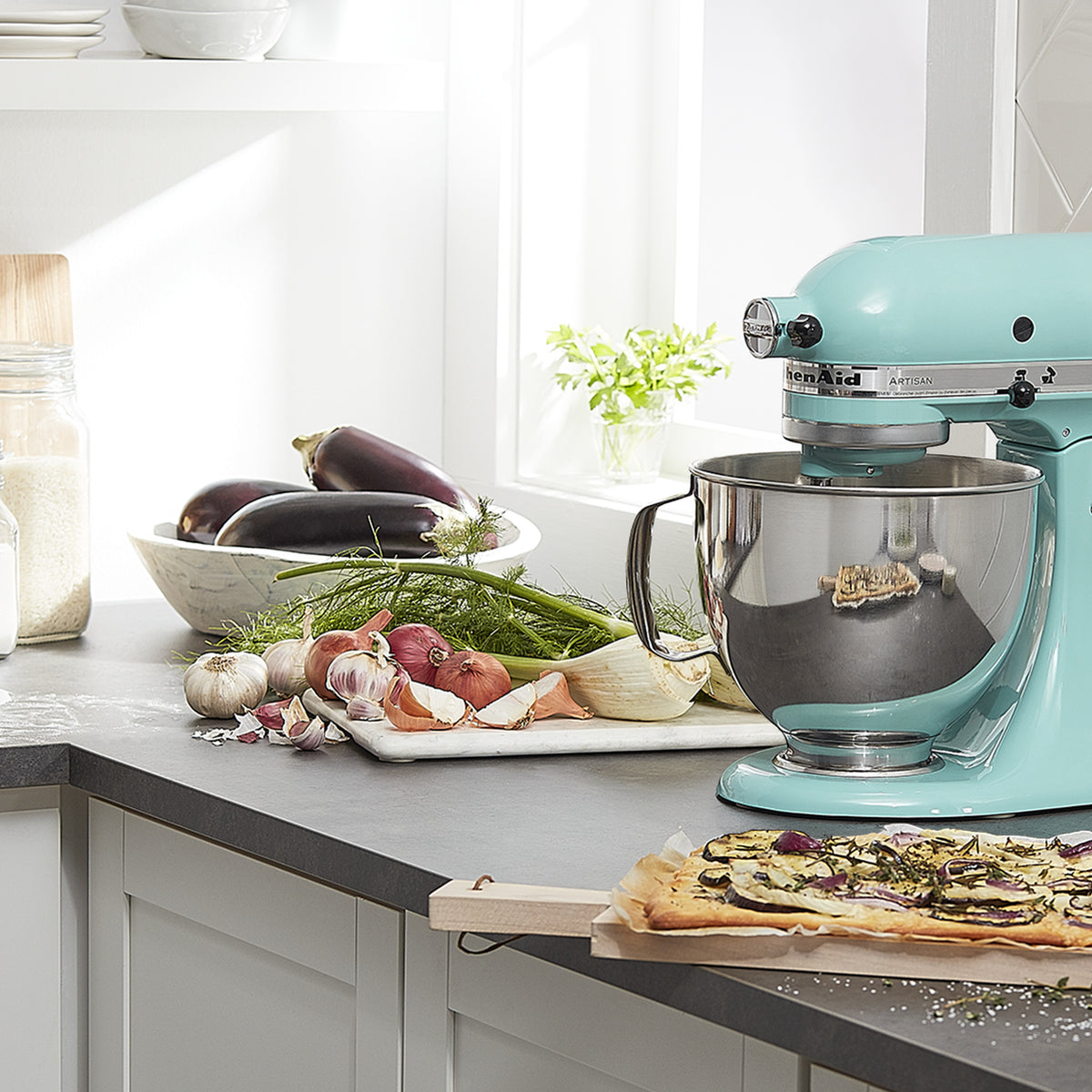 KitchenAid Artisan Series 5-Quart Tilt-Head Stand Mixer in aqua sky, on a kitchen counter with fresh produce and a cutting board