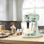 KitchenAid Artisan Series 5-Quart Tilt-Head Stand Mixer in pistachio, on a wooden kitchen counter by a window with baked goods
