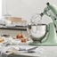 KitchenAid Artisan Series 5-Quart Tilt-Head Stand Mixer in pistachio, on a kitchen counter beside a dessert spread