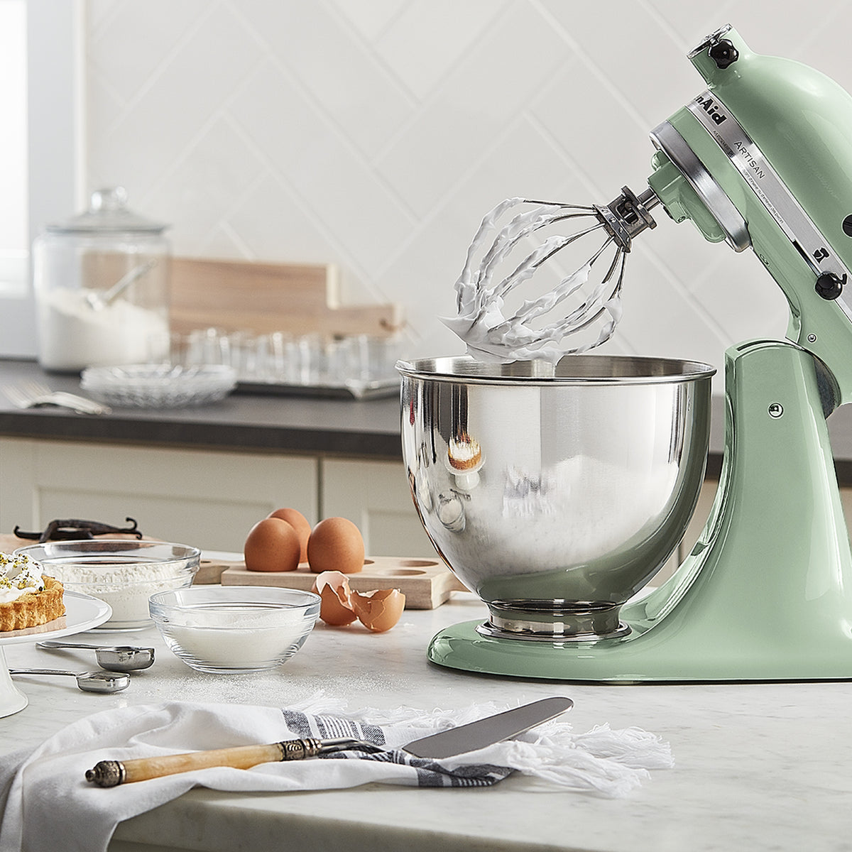 KitchenAid Artisan Series 5-Quart Tilt-Head Stand Mixer in pistachio, on a kitchen counter beside a dessert spread