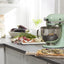 KitchenAid Artisan Series 5-Quart Tilt-Head Stand Mixer in pistachio, on a kitchen counter with fresh produce and a cutting board