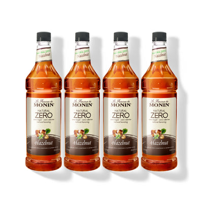 Four 1L plastic bottles of Monin Natural Zero Hazelnut syrup in a row