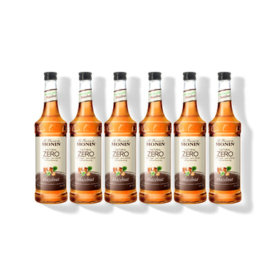 Six 750ml glass bottles of Monin Natural Zero Hazelnut syrup in a row