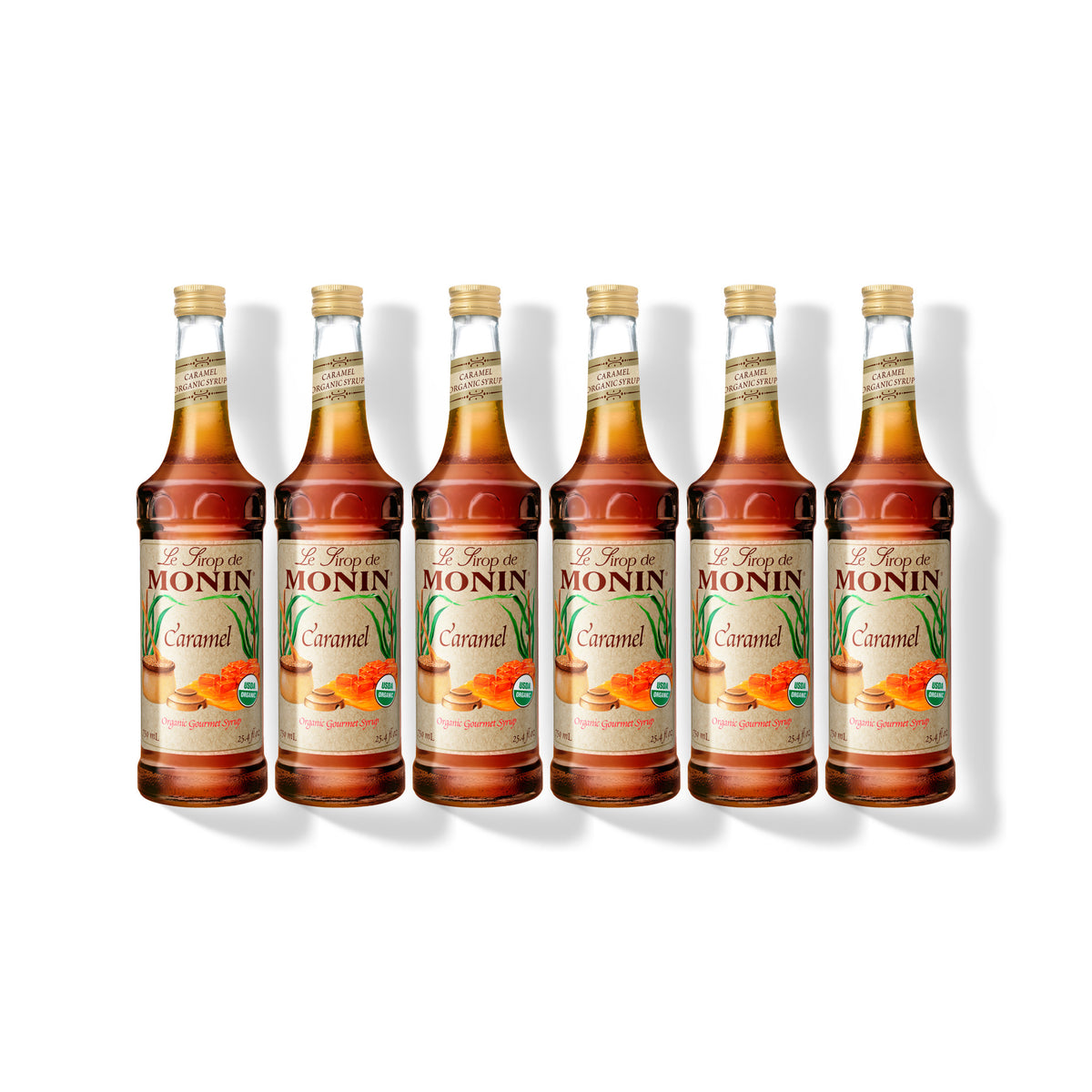 Six 750ml glass bottles of Monin Organic Caramel syrup in a row