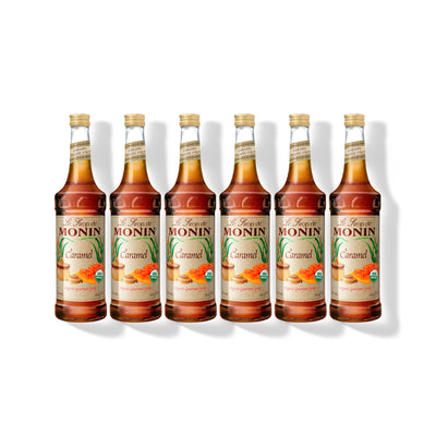 Six 750ml glass bottles of Monin Organic Caramel syrup in a row