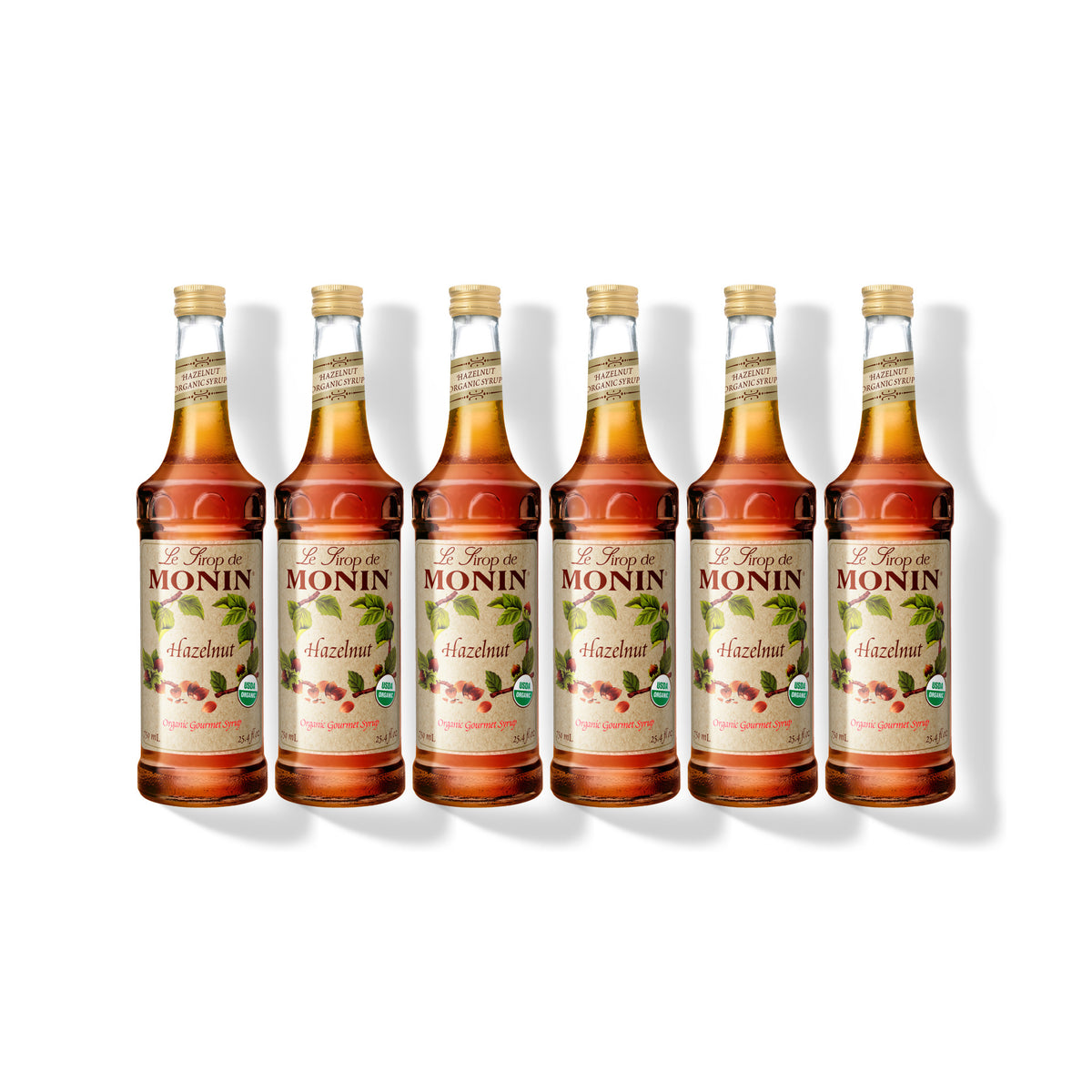 Six 750ml glass bottles of Monin Organic Hazelnut syrup in a row