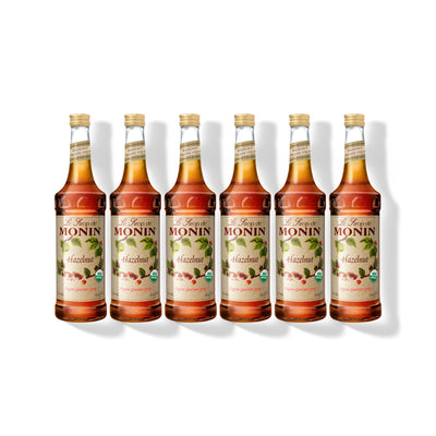 Six 750ml glass bottles of Monin Organic Hazelnut syrup in a row