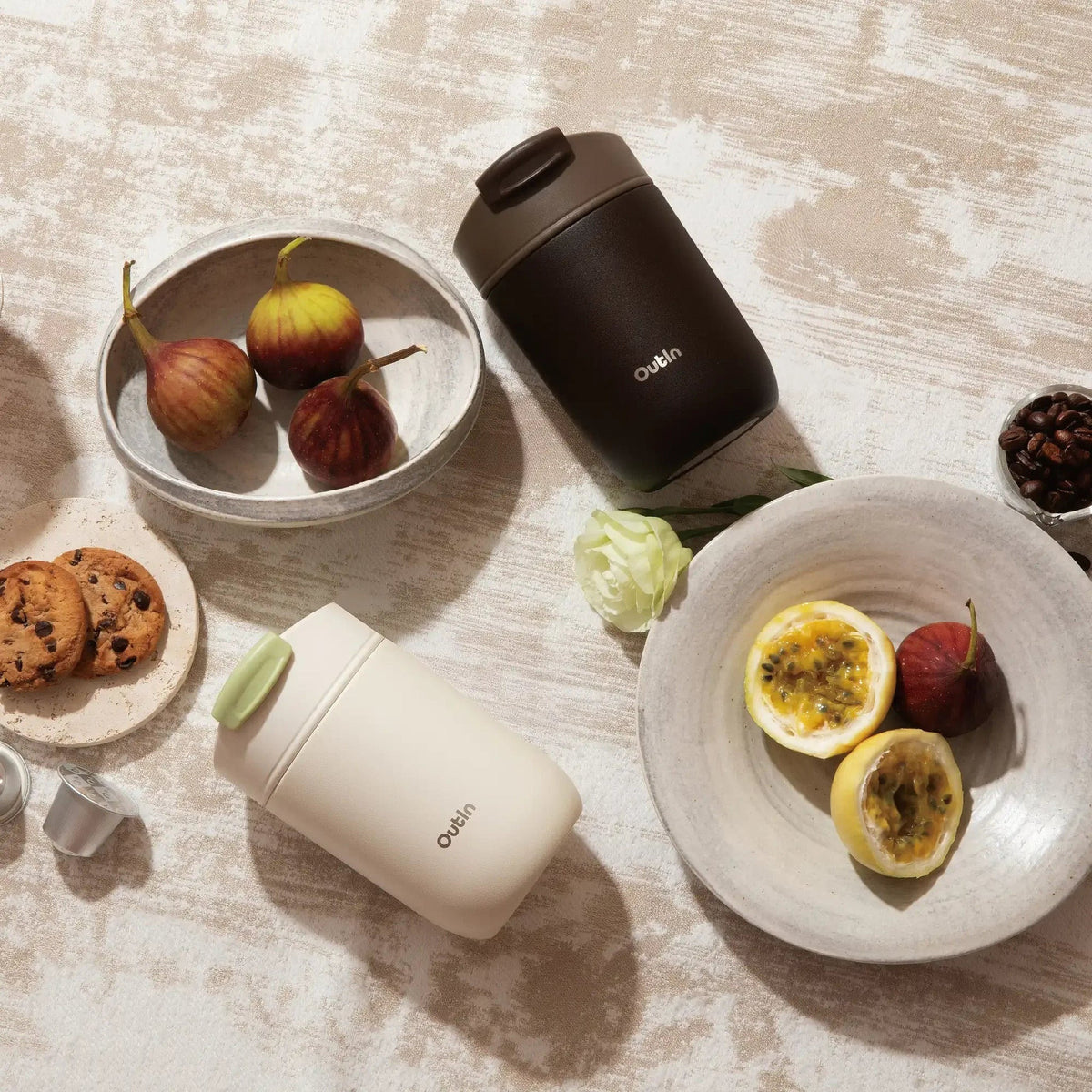 OutIn Travel Tumbler in sand white, on a table with fruit and pastries